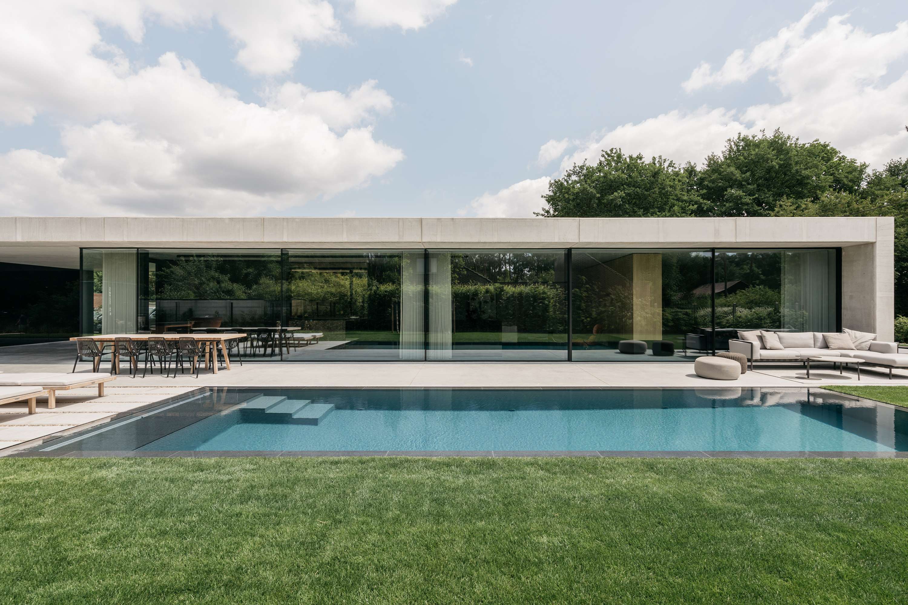 half ondergrondse betonwoning met zwembad mol icoon architecten brasschaat_bungalowwoning beton brede gevel betonnen luifel infinity pool grote ramen
